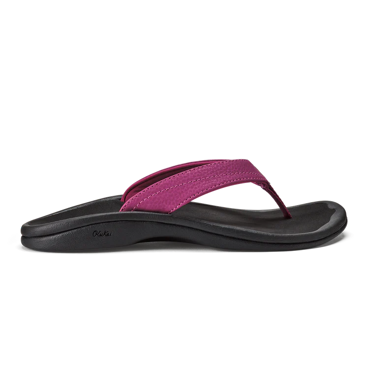 A side view of the OLUKAI W-Ohana Orchid water-resistant sandal, featuring a black sole and a magenta pink thong strap, displayed on a white background.