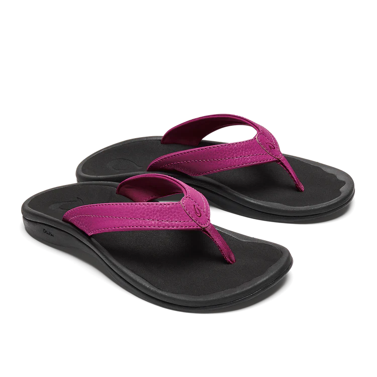 The OLUKAI W-Ohana Orchid features black water-resistant flip-flops with bright pink straps, an anatomical fit, contoured footbeds, and a simple, comfortable design, shown on a white background.