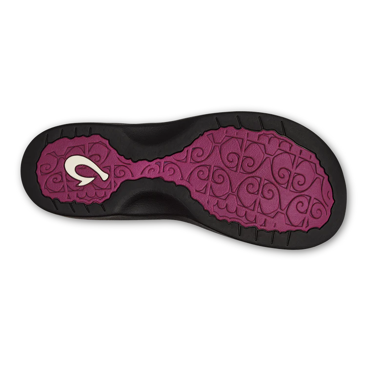 The image shows the sole of the OLUKAI W-Ohana Orchid sandal, with a purple section featuring swirl patterns and a white logo, bordered by black textured edges for anatomical grip.