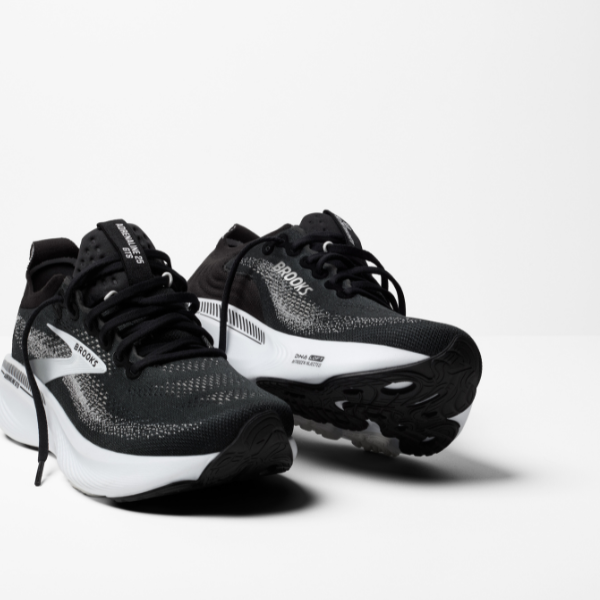 The BROOKS Women's Adrenaline GTS 25 Wide Black/White running shoes feature a black and white design with white soles, visible side branding, and laces—ideal for plantar fasciitis—displayed on a plain white surface.