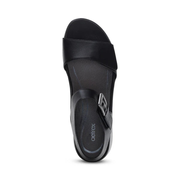 Top view of the Aetrex Women's Ariel Black by AETREX WORLDWide INC, a wedge sandal for foot pain relief with a wide front strap, side buckle, and "Aetrex" branded insole—shown against a white background.