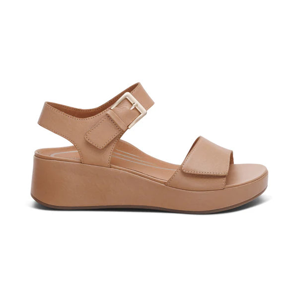 The Aetrex Womens Ariel Sand by AETREX WORLDWide INC is a beige platform sandal with an open toe, Wide front strap, adjustable buckle straps, a low wedge heel, and a textured sole for style and foot pain relief.