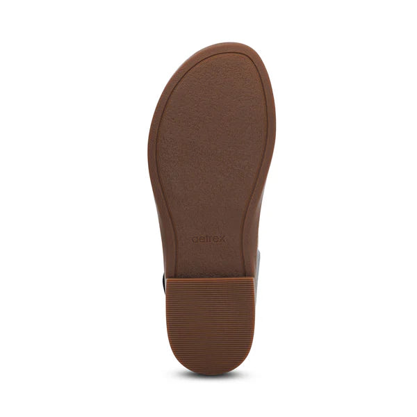 The image shows the bottom view of a black shoe sole with a textured surface and a small rectangular heel. The brand name "AETREX WORLDWide INC" is embossed near the arch, identifying it as the Aetrex Women's Claire Black sandal.