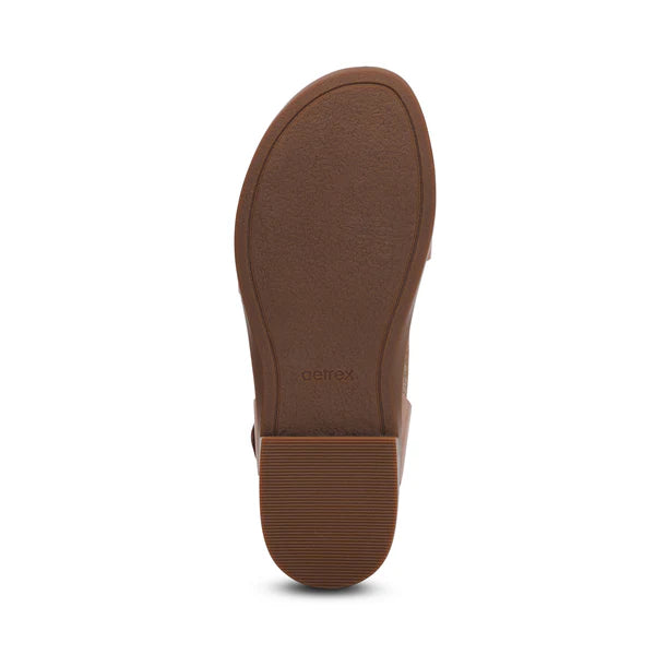 The image displays the bottom view of the Aetrex Women's Claire Cognac sandal by AETREX WORLDWide INC, featuring a brown textured sole, low rectangular heel, and imprinted brand name near the arch—perfect for comfort and arch support.
