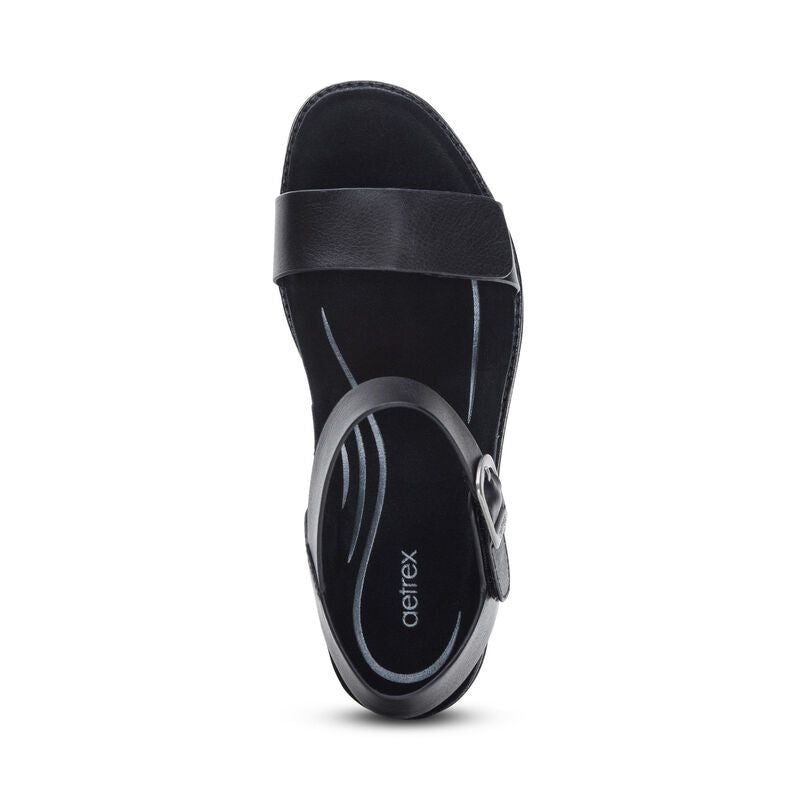 Top view of the Aetrex Womens Mae Black sandal by AETREX WORLDWide INC, featuring a Wide front strap, adjustable quarter strap with buckle, and a cushioned insole with the Aetrex logo and curved grey accents.