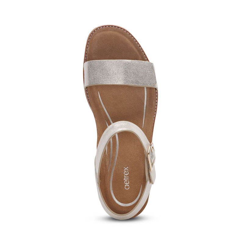 Top view of the Aetrex Womens Mae Champagne sandal by AETREX WORLDWide INC, featuring a champagne leather upper, adjustable quarter strap with buckle at the ankle, cushioned brown footbed, and subtle Aetrex branding.