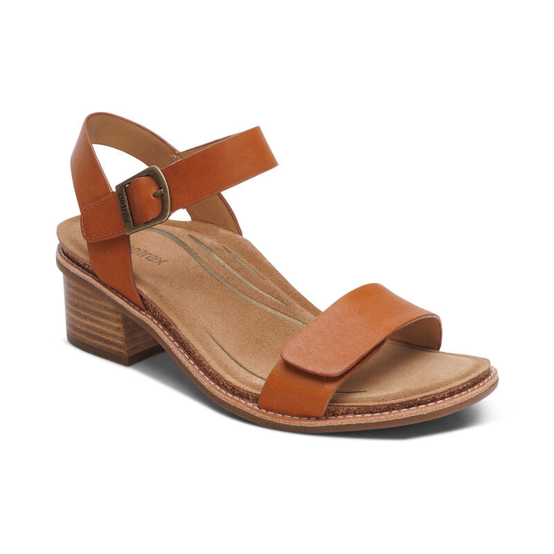 The Aetrex Womens Mae Cognac by AETREX WORLDWide INC offers a brown leather upper, ankle strap with buckle, open toe design, cushioned tan insole, and wood-textured low block heel for stylish comfort.