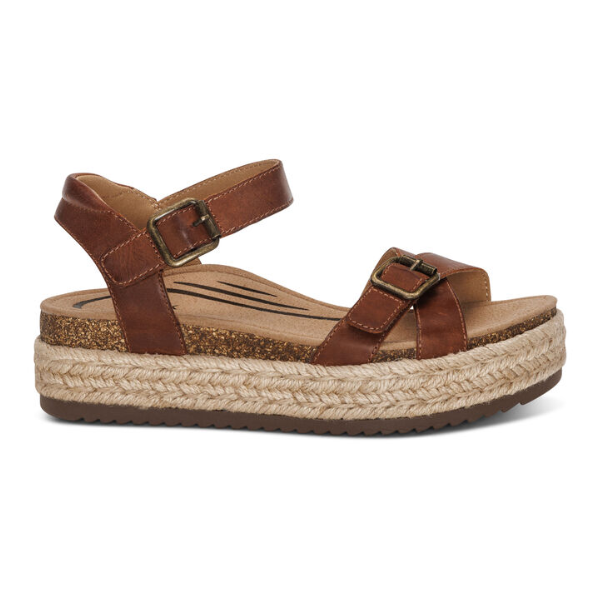 The Aetrex Womens Paula Walnut by AETREX WORLDWide INC is a brown platform sandal with adjustable buckle straps, cork footbed, woven rope midsole, closed heel strap, arch support, and a textured rubber outsole for comfort and stability.