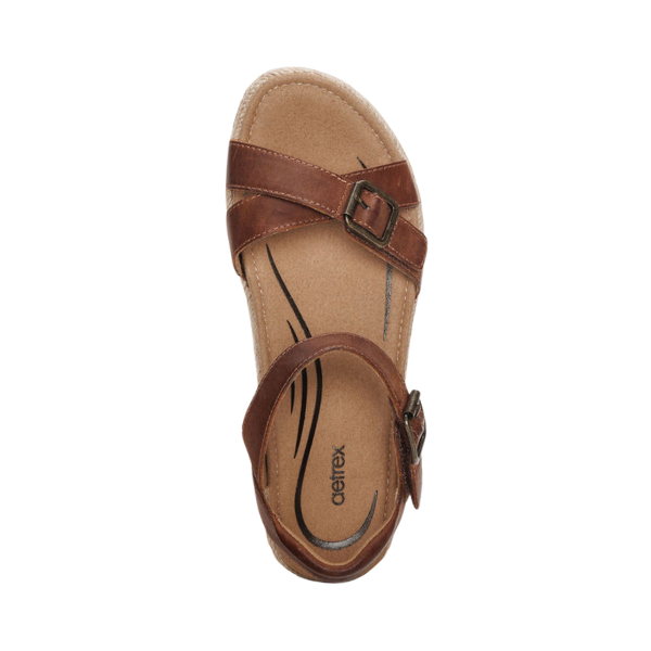 The Aetrex Womens Paula Walnut by AETREX WORLDWide INC features brown straps with two buckles, a cork-textured footbed, and black decorative insole lines—perfect arch support sandals shown from above on a white background.