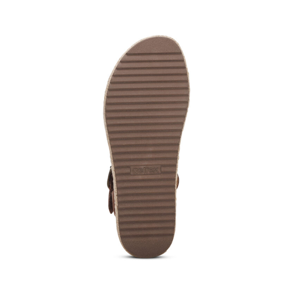 The image shows the bottom view of an Aetrex Womens Paula Walnut sandal by AETREX WORLDWide INC, featuring a brown textured ribbed sole. The design resembles comfort-focused arch support sandals. Background is plain white.