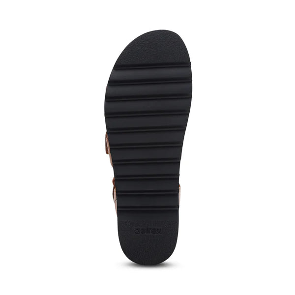 The image shows the bottom view of a black sandal sole with horizontal grooves and Aetrex embossed near the heel, highlighting the anatomical design of the Aetrex Womens Romy Ginger by AETREX WORLDWide INC.