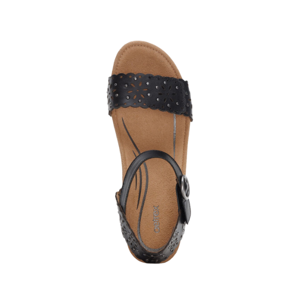 The Aetrex Womens Sydney Black Cutout by AETREX WORLDWide INC is a black open-toe sandal featuring a perforated floral strap and tan cushioned insole with arch support, shown from above on a white background.