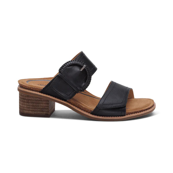 The Aetrex Womens Tatiana Black by AETREX WORLDWide INC is a black open-toe sandal with two straps, a decorative round buckle, low brown block heel, tan insole, and visible stitching for added comfort.