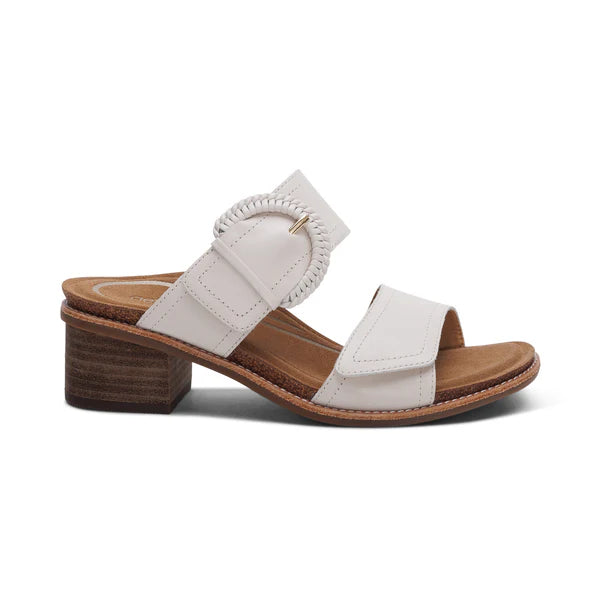 The Aetrex Womens Tatiana Ivory by AETREX WORLDWide INC is a white leather sandal featuring an open toe, Wide front strap, adjustable hook & loop closures, a statement buckle on the ankle strap, low brown block heel, tan lining, and light brown trim.