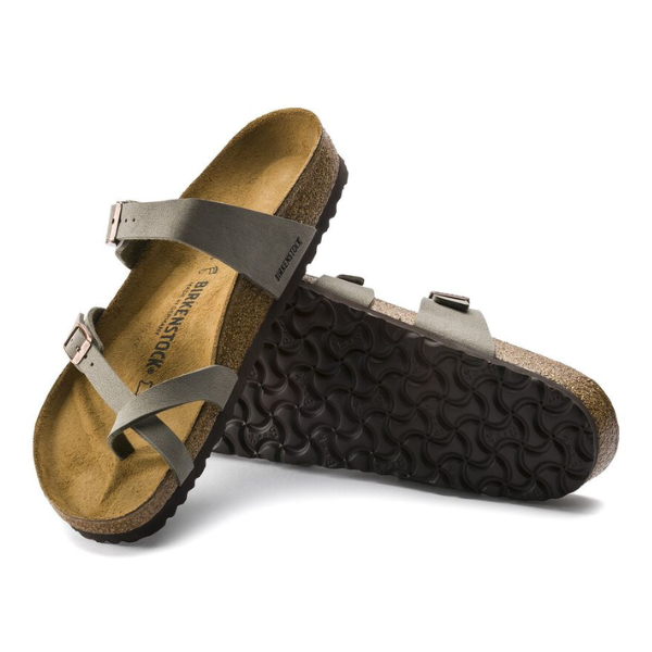 A pair of BIRKENSTOCK Womens Mayari Stone sandals with contoured footbeds and cork soles; one lies flat to show the suede insole and straps, while the other is propped up, revealing the textured black rubber outsole.