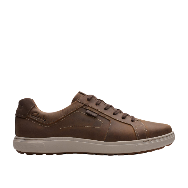 The Clarks Mens Mapstone Lace Wide Beeswax by CLARKS is a casual brown beeswax leather sneaker with brown laces, visible tan stitching, white rubber sole, and supportive cushioning. Shown low-top and photographed from the side on a white background.