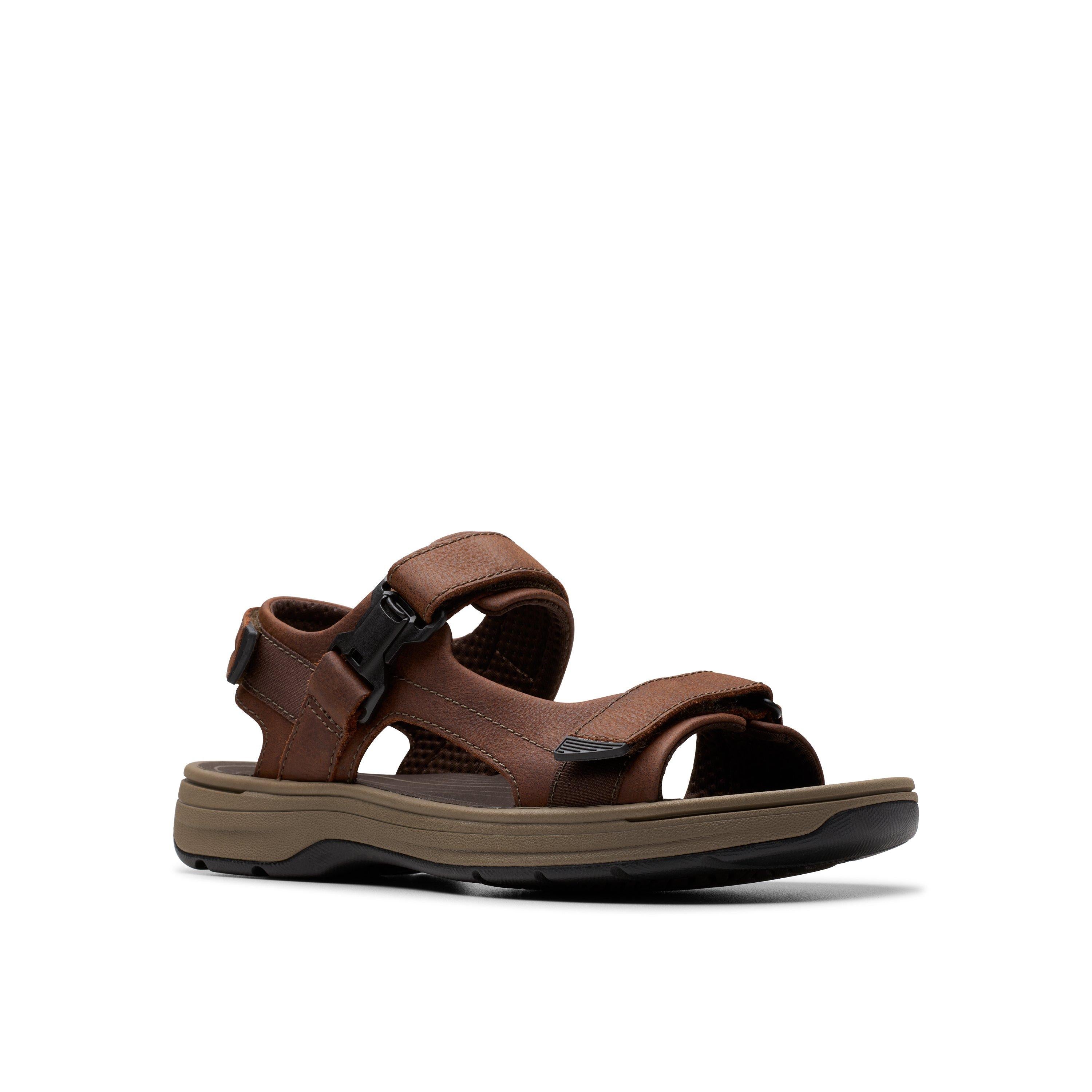 The CLARKS Mens Saltway Edge Wide Brown sandal features brown leather with adjustable straps, visible stitching, a thick EVA sole, and a black side buckle, shown against a plain white background.