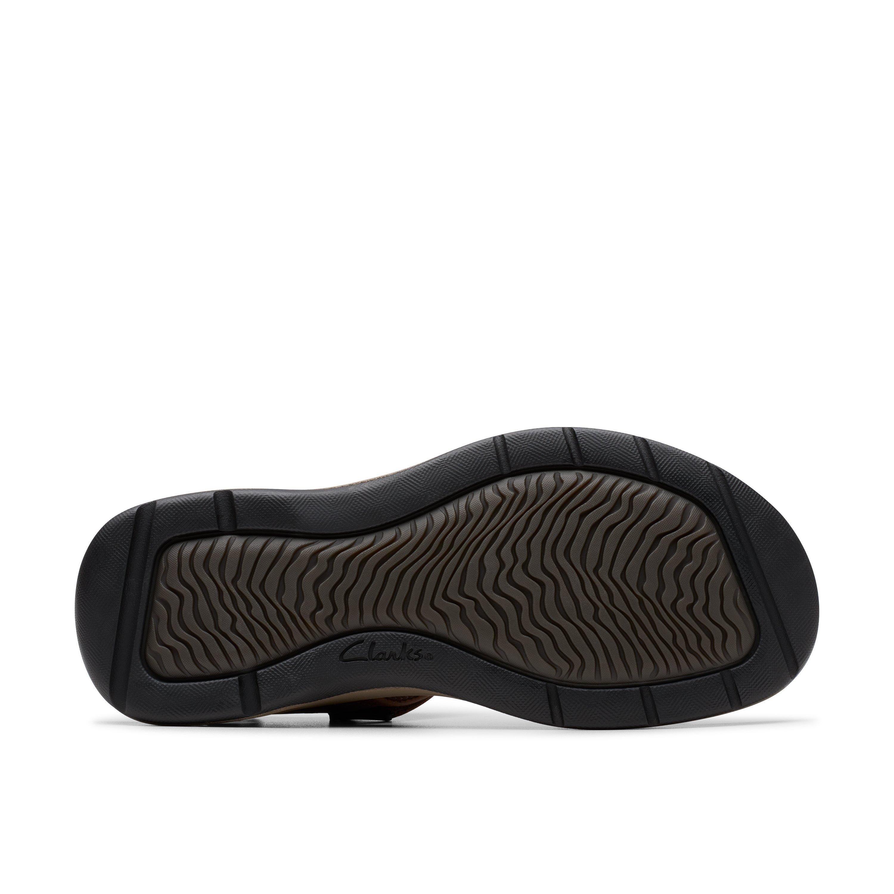 The image shows the bottom view of a CLARKS Mens Saltway Edge Wide Brown sandal, featuring a black and gray EVA sole with a wavy tread and the CLARKS logo embossed near the heel.