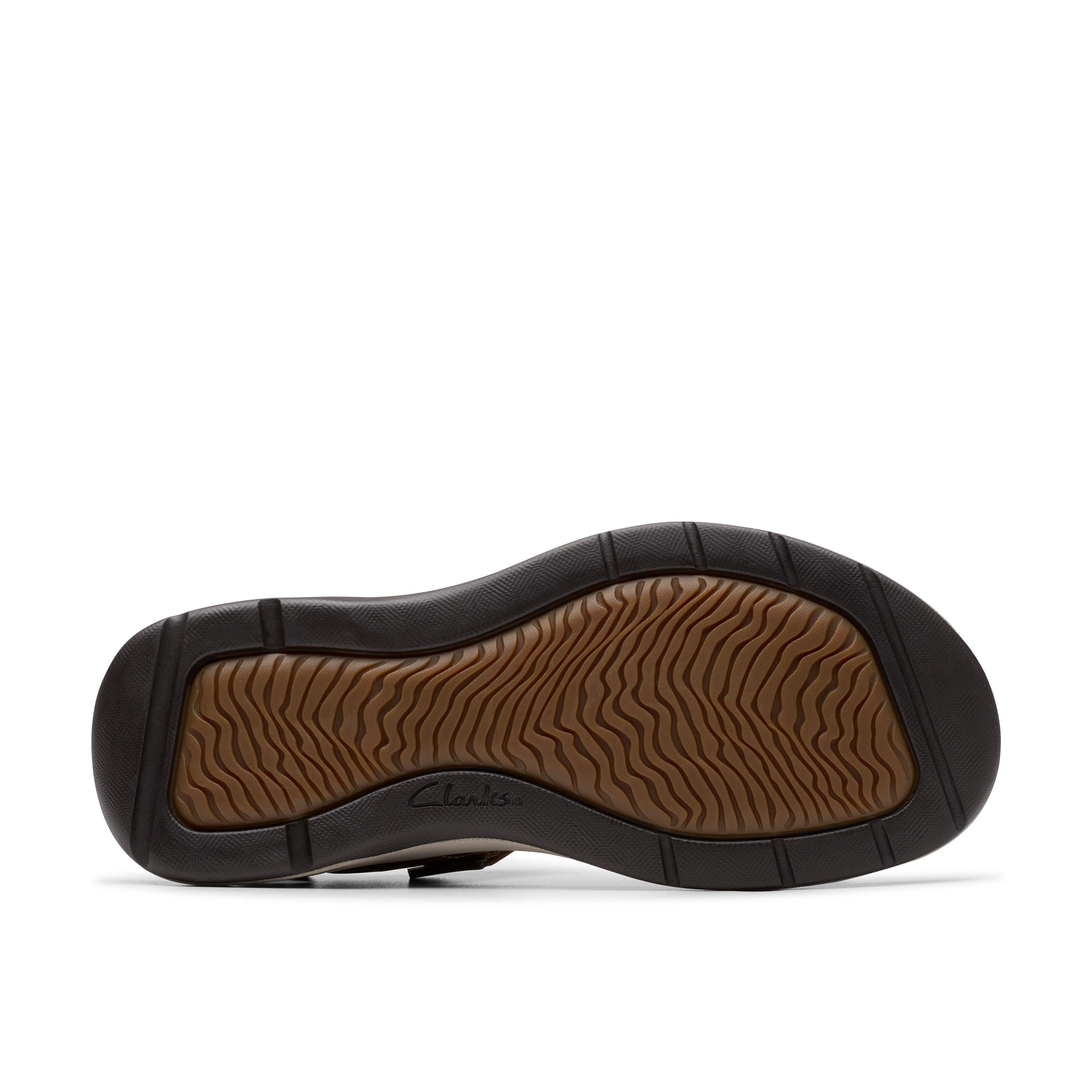 The image displays the sole of a CLARKS Mens Saltway Edge Wide Tan sandal, featuring a wavy, textured brown tread with a black border and the CLARKS logo embossed, complemented by classic light tan leather.