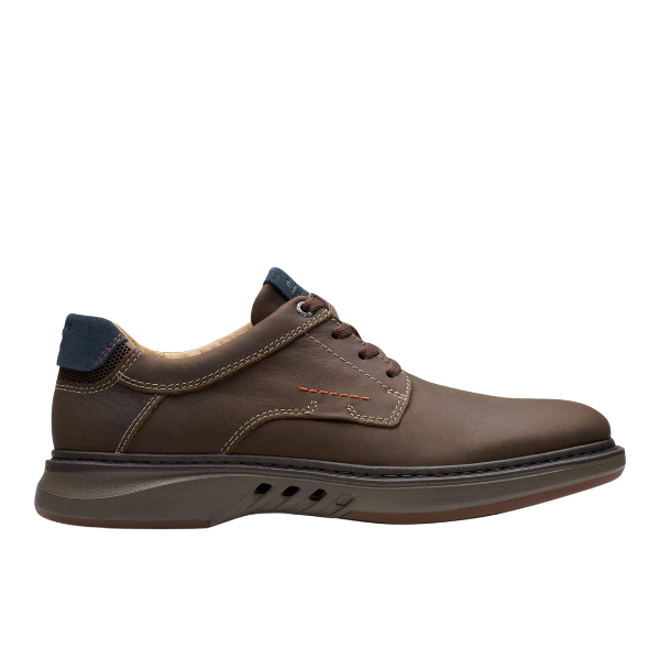 The Clarks Mens Un Briley Pace Wide Brown by CLARKS is a brown leather lace-up casual shoe with nubuck upper, dark blue heel accents, visible stitching, thick curved rubber sole, and contoured footbed for support. Shown in profile on white background.