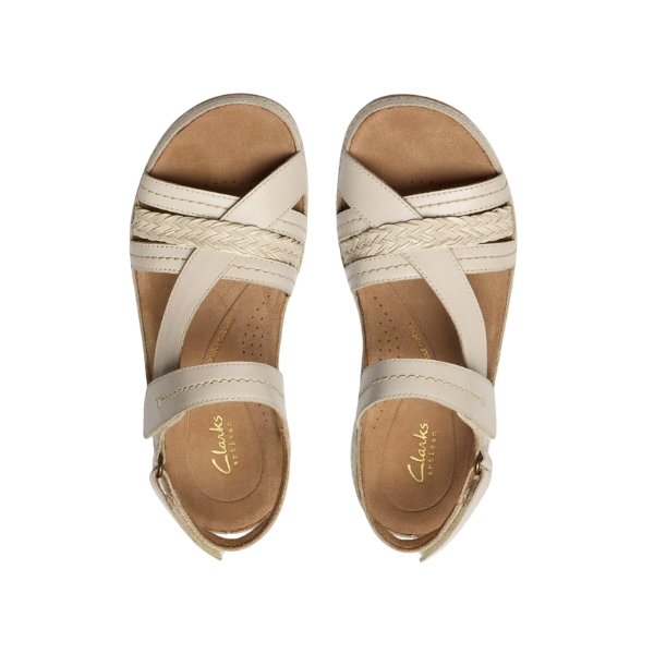 A pair of CLARKS Womens Cecily Strap Leather Wide Cream sandals with braided and smooth straps, ankle buckles, and a Contour Cushioned Footbed, viewed from above on a white background.