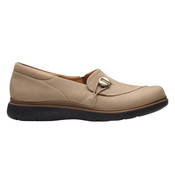 The CLARKS Certina Ease Wide Pebble is a womens beige slip-on loafer with pebble nubuck, a rounded toe, decorative strap and metallic button, removable footbed, and thick black sole—ideal for all-day comfort.