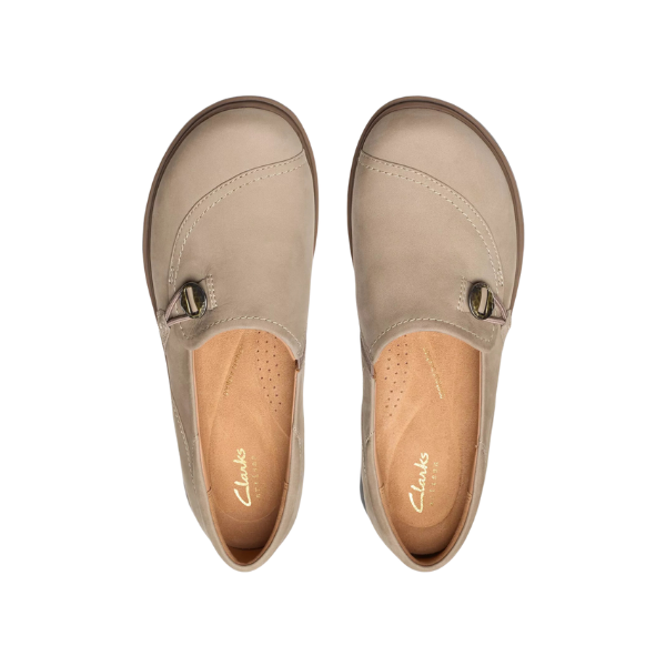A pair of CLARKS Womens Certina Ease Wide Pebble slip-on shoes in taupe nubuck, featuring a round toe, side buckle detail, and visible stitching, shown from above on a white background.