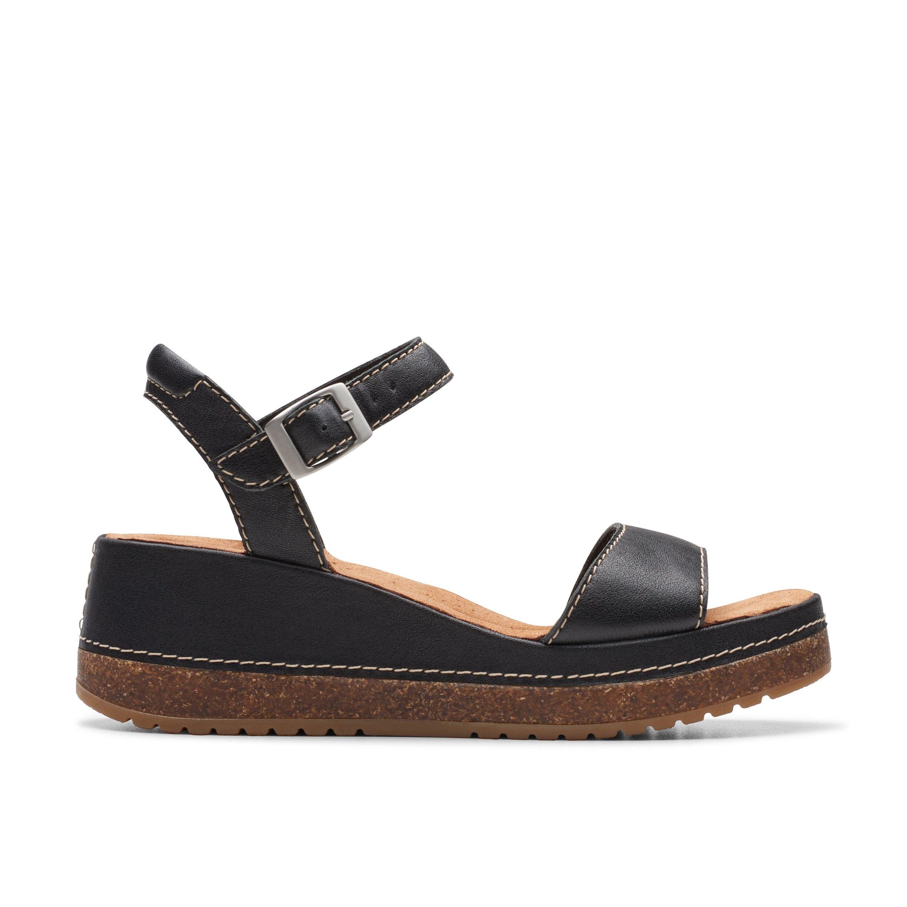 The CLARKS Womens Kassandra Lily Black sandal features an open toe, ankle strap with buckle, white stitching, and a cork-effect wedge heel. Its Contour Cushion footbed adds comfort. Shown from the side against a white background.