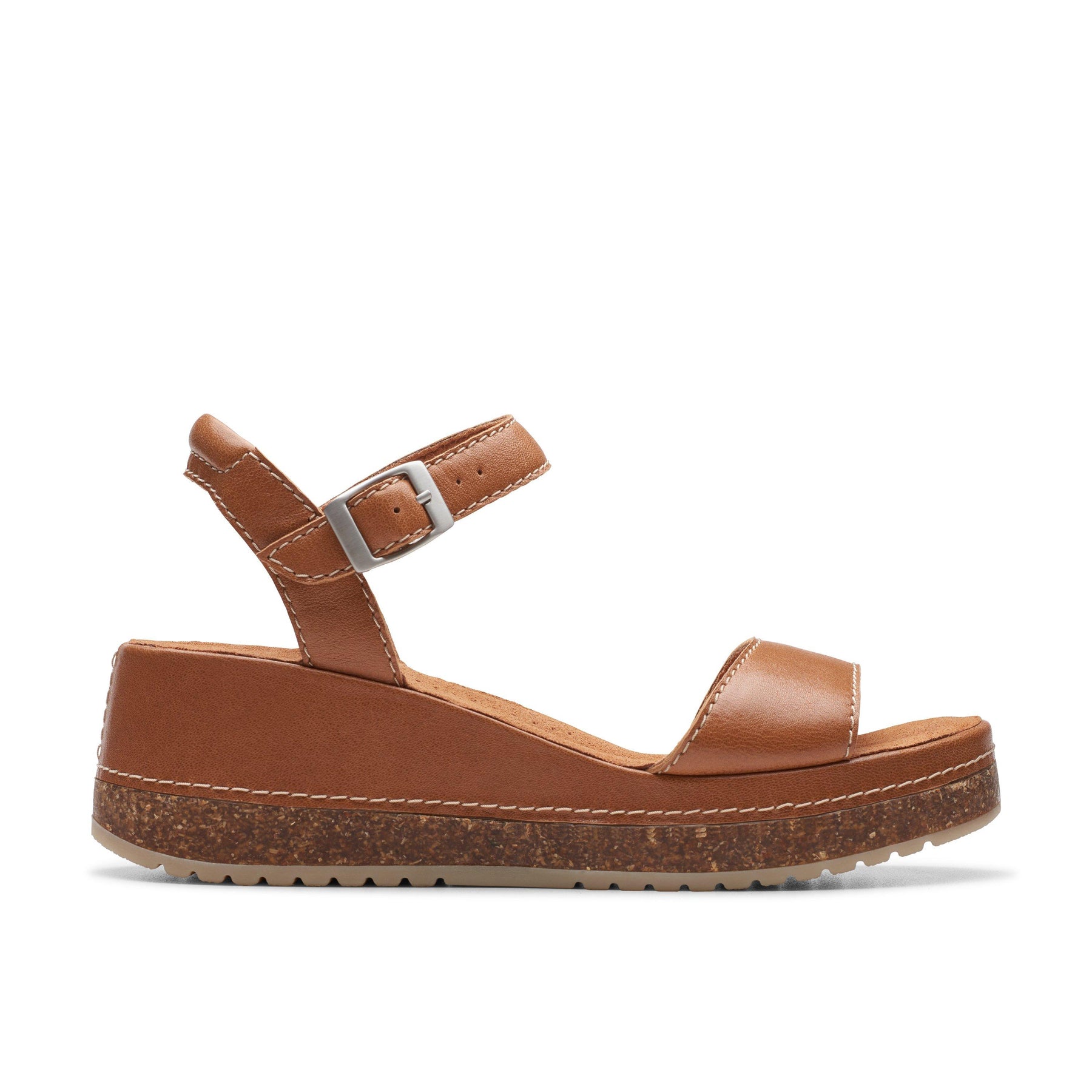 The Clarks Womens Kassandra Lily Wide Tan sandal features premium tan leather, an ankle strap with buckle, cork-textured wedge sole, white edge stitching, and a Contour Cushion footbed—all by CLARKS, shown in side profile on white.