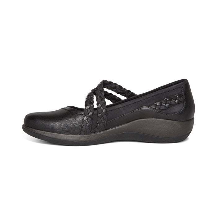 The Aetrex Womens Annie Mary Jane Black by AETREX WORLDWide INC is a black slip-on flat with braided straps, a slightly elevated sole, arch support, and comfort ideal for plantar fasciitis. It features a rounded toe and braided side detail.