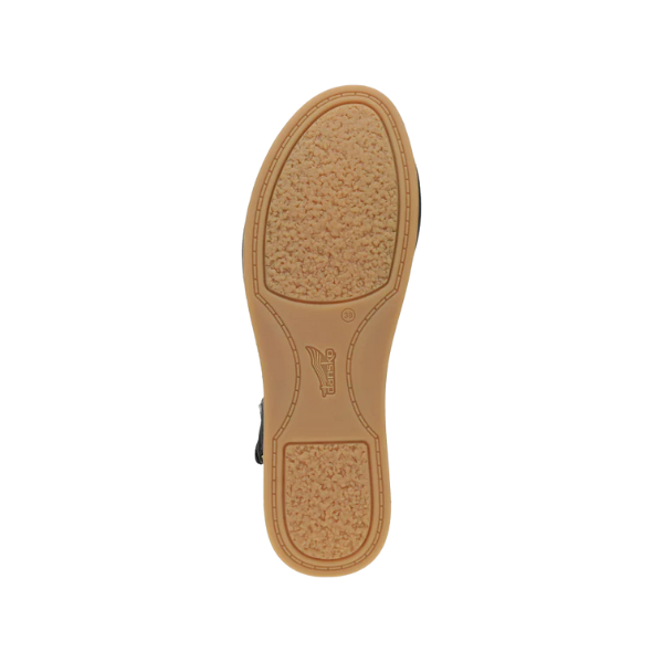 The image displays the bottom view of the Dansko Womens Cass Black Nubuck shoe by DANSKO, highlighting its textured tan sole with a central brand logo and cork midsole for foot pain relief, all set against a white background.