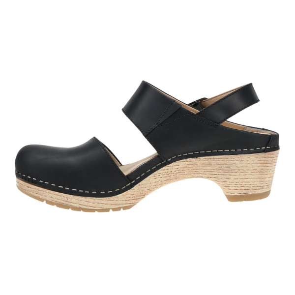 The Dansko Womens Lucia Black by DANSKO is a closed-toe, heeled clog with black leather, open heel, adjustable strap, and white stitching on a light wood-textured platform—ideal for comfort and foot pain relief.