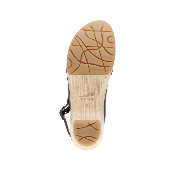 Top view of the Dansko Womens Lucia Black sandal shows a tan, textured, wavy sole with the DANSKO logo. Inspired by the Lucia clog, it features black side straps, a slight heel, and provides comfort for foot pain.