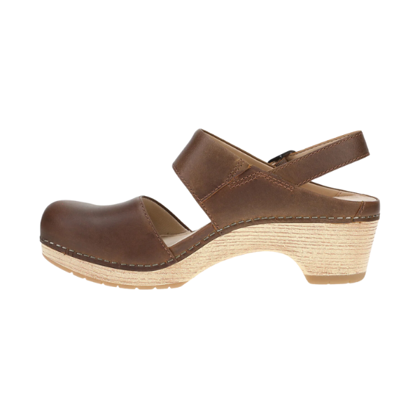 The DANSKO Womens Lucia Tan is a brown leather closed-toe clog with a Wide strap, open back and ankle strap, light wood-textured medium heel, and visible sole stitching—ideal for stylish comfort.