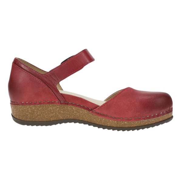The Dansko Womens Mae Red Suede by DANSKO is a Mary Jane-style shoe with lightweight EVA and cork soles, low wedge heel, closed toe, adjustable strap, visible edge stitching, and a durable rubber outsole.