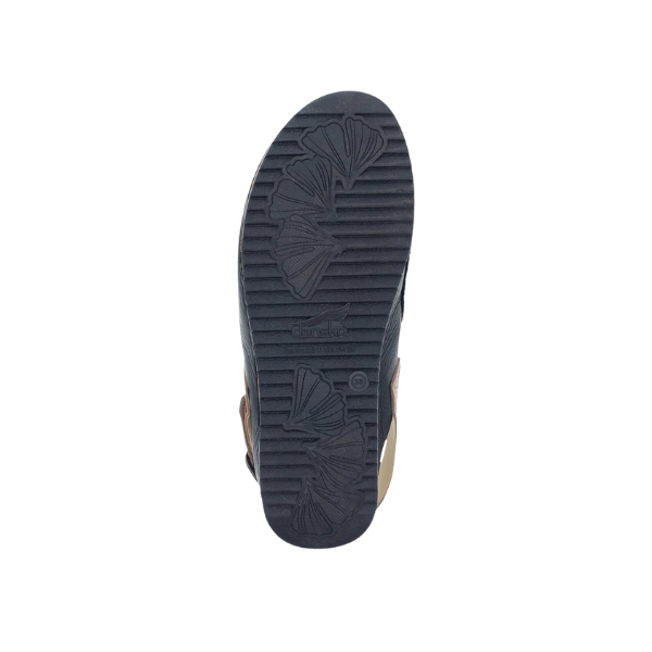 The image displays the bottom view of a Dansko Womens Merrin Black shoe by DANSKO, highlighting its dark sole with grooved and leaf-like patterns for odor control, set against a white background.