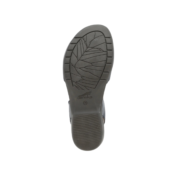The bottom view of the Dansko Womens Rowan Black Waxy sandal shows a black sole with a leaf-patterned tread, horizontal grooves for support, and the DANSKO brand name visible near the center.