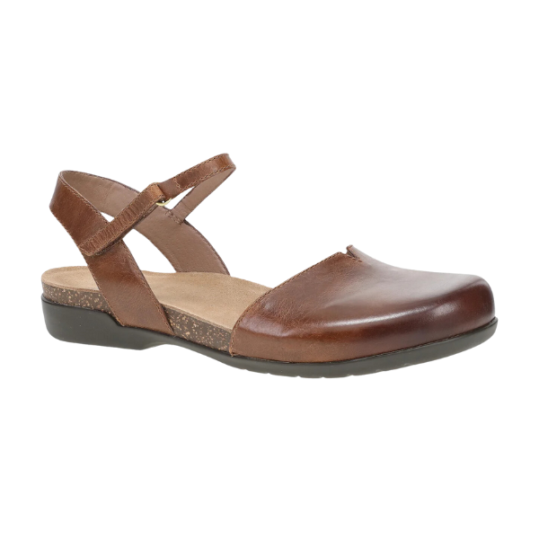 The Dansko Womens Rowan Tan by DANSKO is a brown leather flat with a closed toe, open heel, cross-strap buckle, memory foam insole for foot pain relief, and a low black sole.