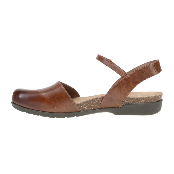 The Dansko Womens Rowan Tan by DANSKO is a brown leather shoe with a closed toe, open sides, ankle strap, flat sole, low heel, cork insole accent, and memory foam for foot pain relief.