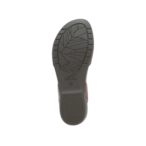 The image shows the sole of the Dansko Womens Rowan Tan shoe by DANSKO, with a leaf-patterned tread and central logo. It features a memory foam insole for exceptional foot pain relief.