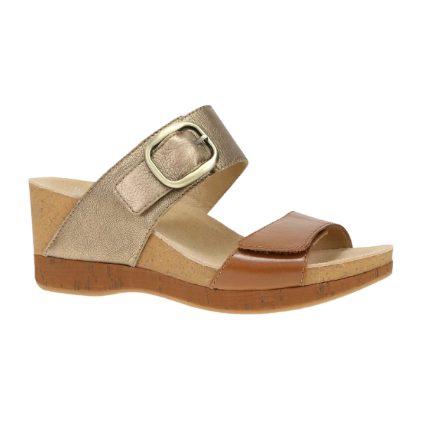 The Dansko Womens Shannon Gold/Tan wedge slide sandal by DANSKO features a cork sole, brown leather toe strap, and metallic gold ankle strap with a large gold buckle—combining style with foot pain relief.