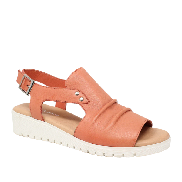 The Django & Juliette Womens Madis Melon sandal features a melon color, open toe, slingback buckle strap, flexible wedge sole with white ridges, and decorative silver side studs.