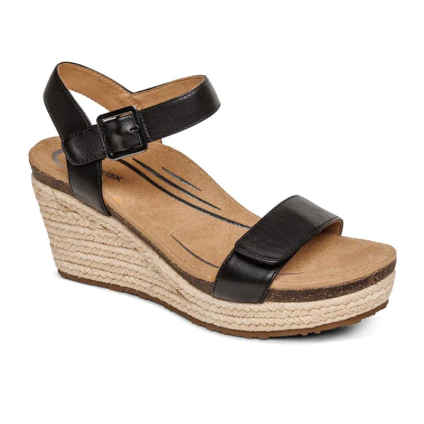 The Aetrex Womens Sydney Black Leather sandal features a buckle ankle strap, tan cushioned insole with arch support, and a textured espadrille-style platform sole.