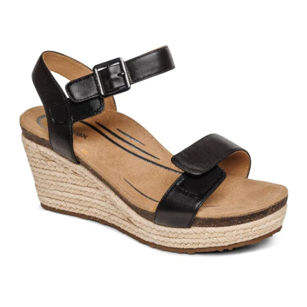The Aetrex Womens Sydney Black Leather sandal features an ankle strap, buckle closure, and memory foam footbed for comfort, plus stylish black detailing on a tan insole and a platform heel wrapped in braided jute.