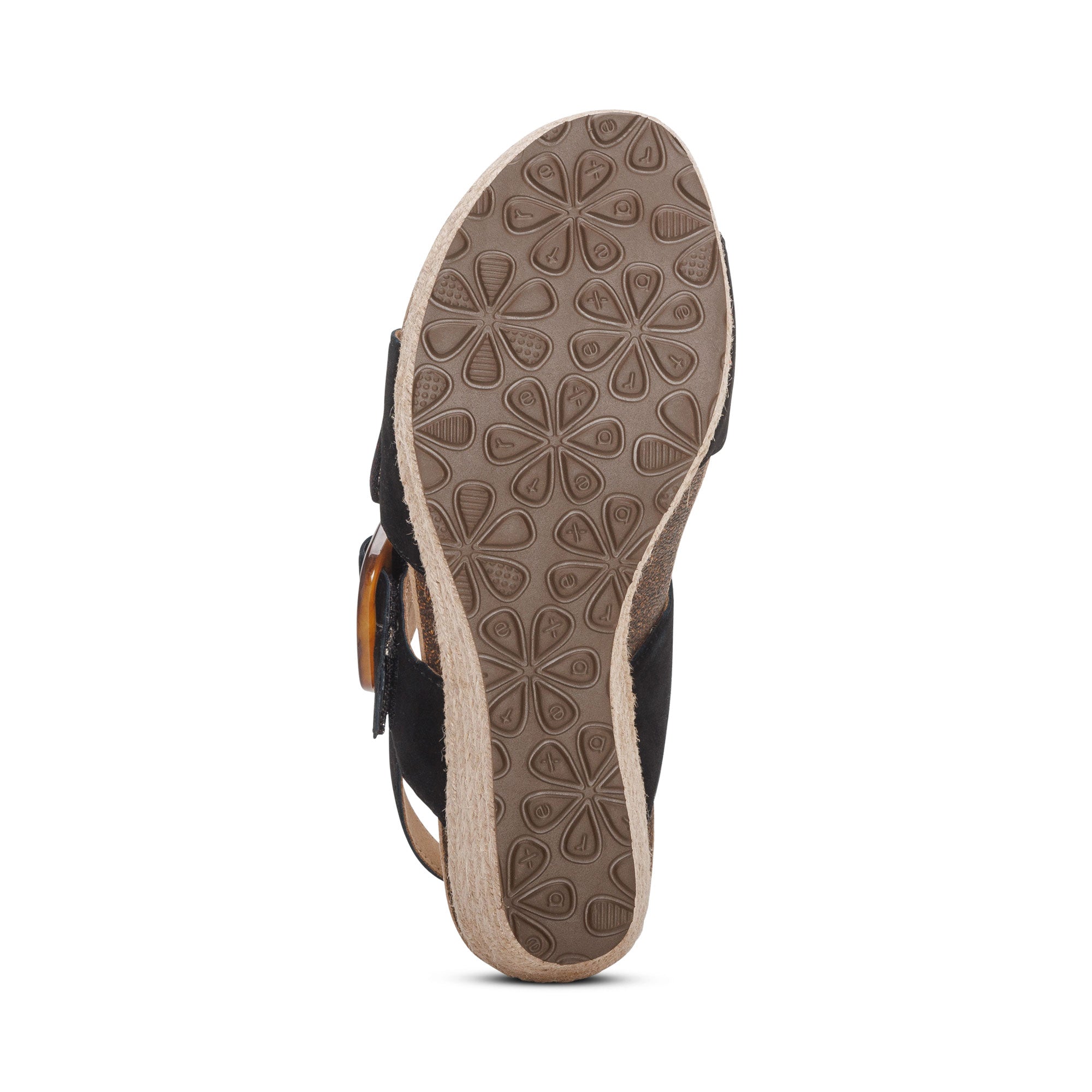 The image shows the bottom view of the Aetrex Women's Ashley Espadrille Wedge Black by AETREX WORLDWide INC, featuring a textured rubber sole with a floral geometric pattern, arch support wedge, and black upper with a side buckle.