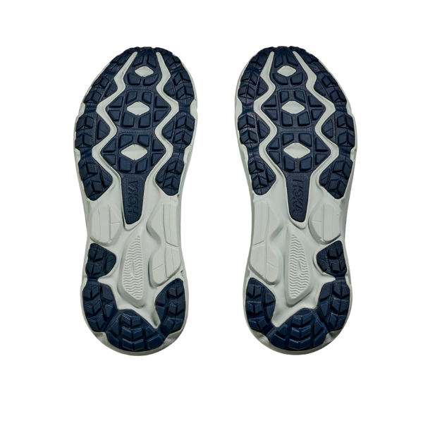 A pair of HOKA Womens Challenger ATR 7 Wide Aqua soles face upward, showing a white base with dark blue textured rubber tread and Meta-Rocker tech for grip, displayed on a plain white background.