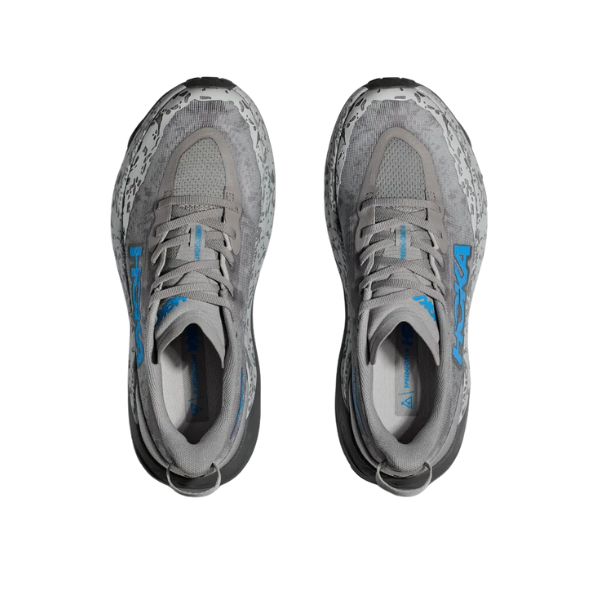 Top view of HOKA Womens Speedgoat 6 in Stellar Grey/Asteroid Wide with speckled Vibram Megagrip soles, blue side logo, and gray laces. Shoes are side by side on white—perfect for trail running.