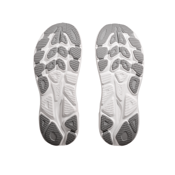 Two HOKA Mens Clifton 10 Wide Grey sneakers are displayed sole up on a white background, highlighting their tread patterns and cushioned design for foot pain relief.