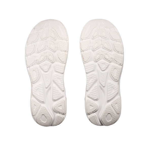 A pair of HOKA Womens Clifton 10 White shoes displays their textured, geometric tread soles against a white background—ideal for those craving plush performance and cushioning.