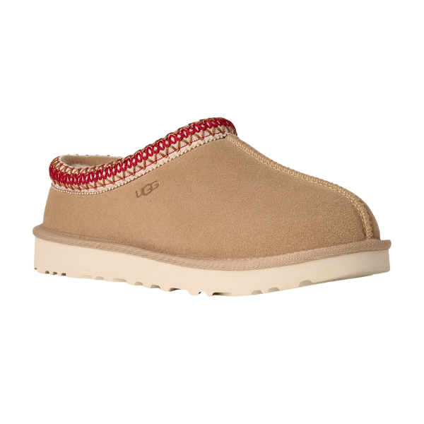 The UGG Women's Tasman II Sand is a tan suede slide with a cream rubber sole, red and white trim along the collar, and an embossed UGG logo—a stylish twist on classic women’s sheepskin slippers.